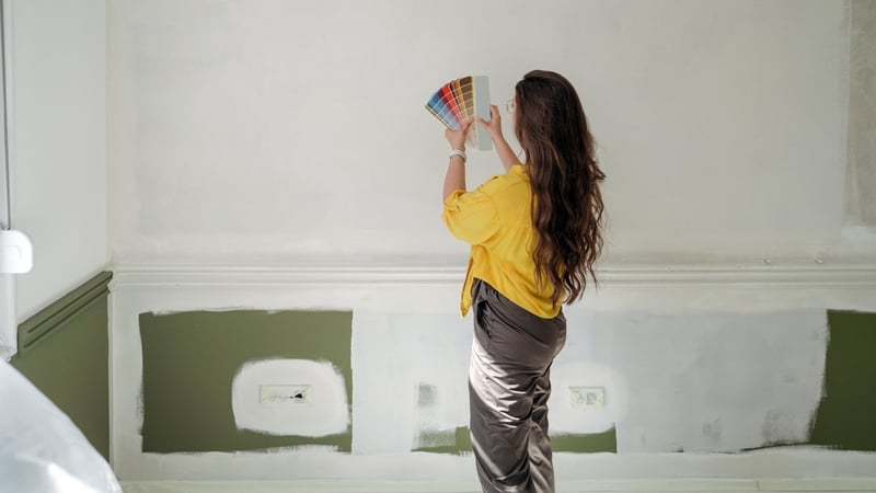 Photo of a woman choosing a paint shade for a wall in her apartment, from a colour palette (colour swatch)