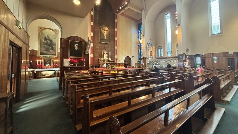 Several brown benches can be seen inside a church. The windows are colourful stained glass.