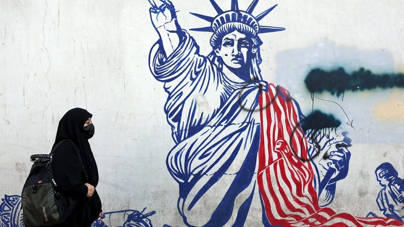 A veiled Iranian woman walks past an anti-US mural next to former US embassy in Tehran