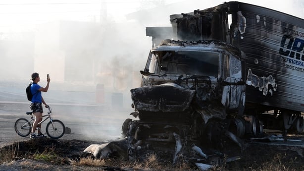 A man riding a bicycle takes a photo of a burned truck, allegedly set on fire by organised crime groups near Acatlan de Juarez, Mexico