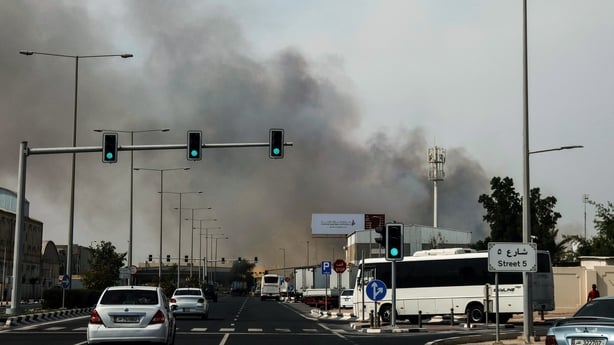 Motorists drive past a plume of smoke rising from a reported Iranian strike in the industrial district