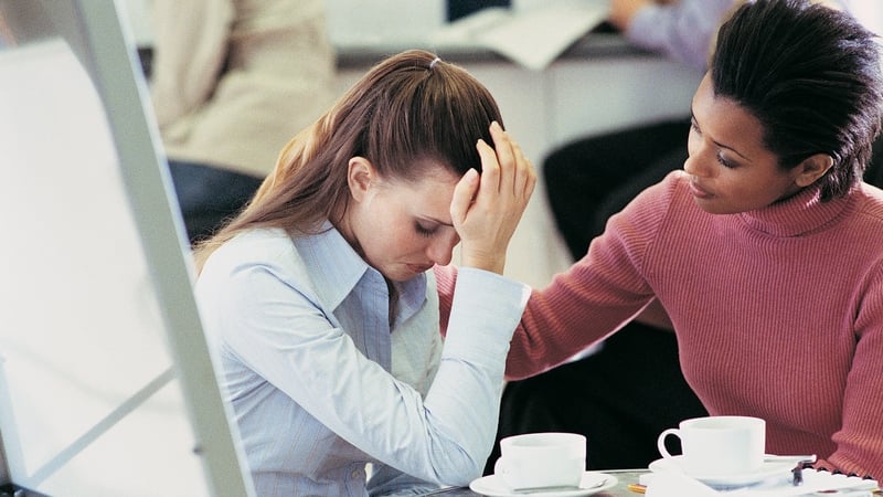 Tearful Businesswoman Being Consoled by a Colleague Sitting at a Table in an Office Canteen
