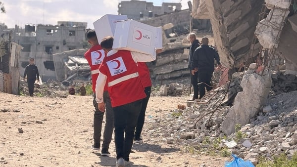 Two red cresent workers carry boxes of aid in a ruined part of Gaza