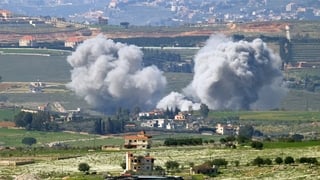 Smoke from a bombardment rises above a settlement in a rural location