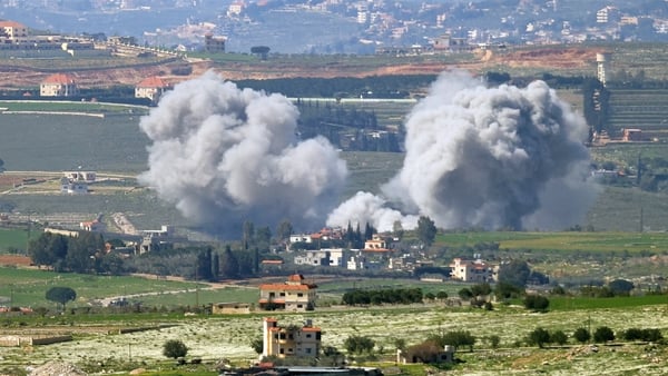 Smoke from a bombardment rises above a settlement in a rural location