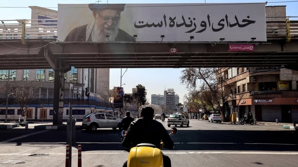Iranians drive past a banner bearing a portrait of Iran's slain supreme leader Ayatollah Ali Khamenei and reading in Persian "His God is still alive" in Tehran on March 3,