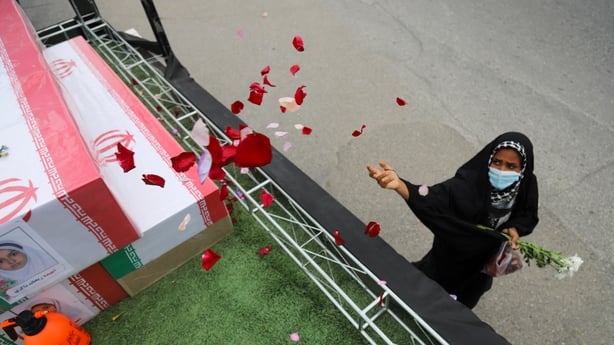A mourner sprays flower petals on the coffins of children 