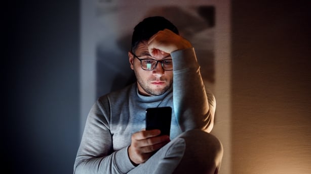 A 35-year-old guy is sitting in the dark room and using his smartphone.