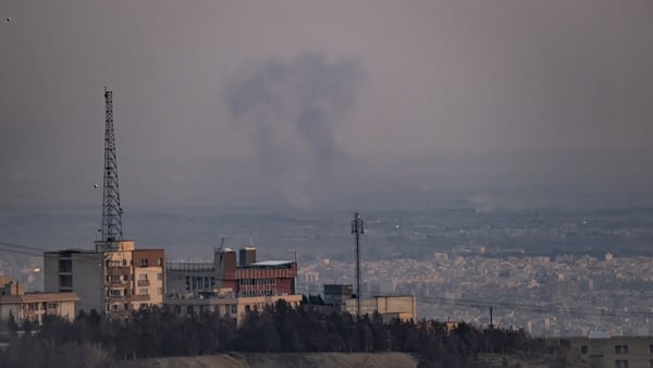 a plume of smoke is seen rising in the distance over a city