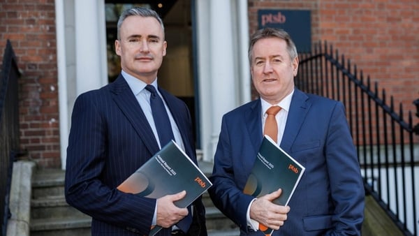 Two business men pose in front of an office with annual results in their hands