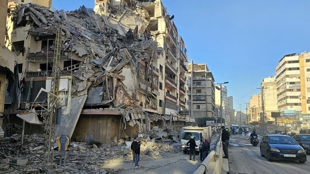 People gather amid the debris of a destroyed building following airstrikes in Beirut's
