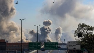 Motorists drive along an expressway as plumes of smoke rise after a strike in Tehran