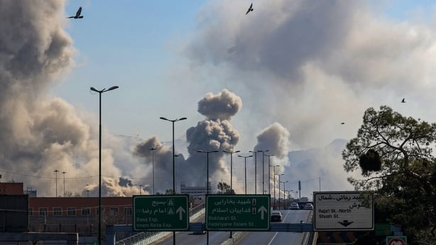 Motorists drive along an expressway as plumes of smoke rise after a strike in Tehran