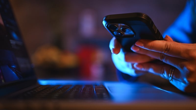 Person using mobile phone and computer at night with glowing blue screen light