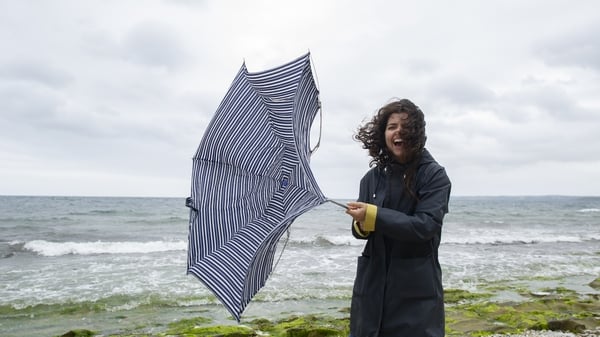A woman standing by the sea with an umbrella on a very windy day