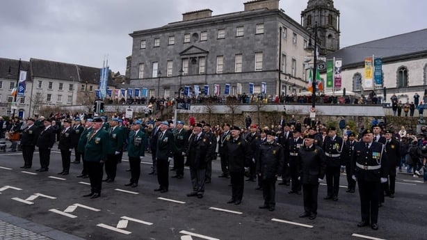 Men in uniform stand to attention on a road in Waterford City as crowds look on