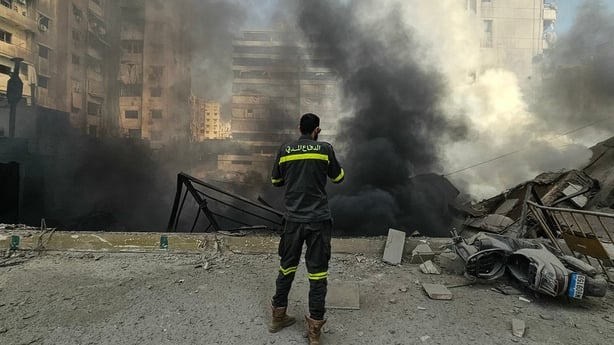 A man in uniform looks at black smoke rising above rubble in beirut
