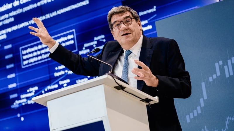 Image of a banker speaking at a podium with graphs behind him