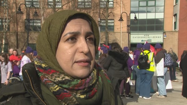 Iranian academic and activist Azadeh Sobout speaking to camera with a protest gathering behind her