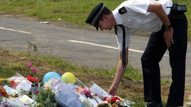 A Police officer lays flowers on a floral tribute near the crime scene of the murdered 10 year-old schoolgirls Holly Wells and Jessica Chapman on the perimeter of Lakenheath RAF airbase 19 August 2002, some 100 miles (160 km) north of London. College caretaker Ian Huntley, 28, and his companion Maxi