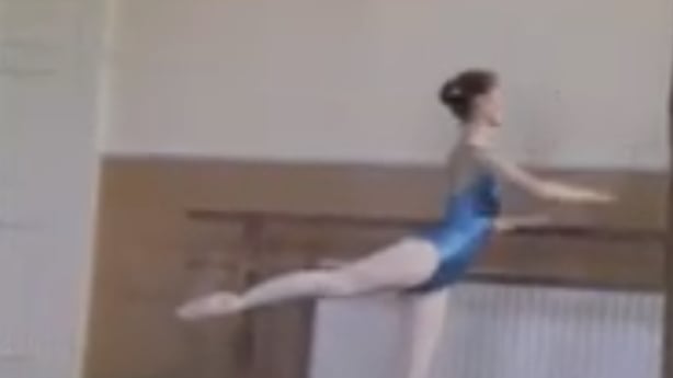 Young woman standing at the barre in leotard and ballet shoes