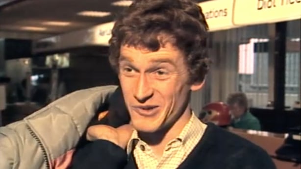 Dark haired man holding coat over his shoulder