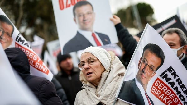 an older woman holding a flag bearing the image of jailed Istanbul Mayor Ekrem Imamoglu demonstrates with others outside the Marmara-Silivri Prison a