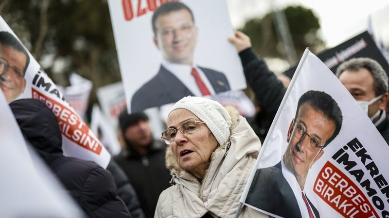 an older woman holding a flag bearing the image of jailed Istanbul Mayor Ekrem Imamoglu demonstrates with others outside the Marmara-Silivri Prison a