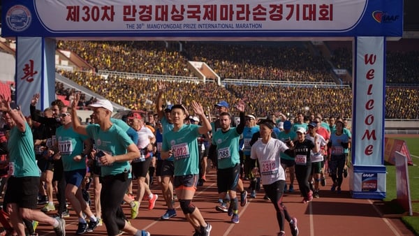 runners cross a start line in a stadium during a marathon race