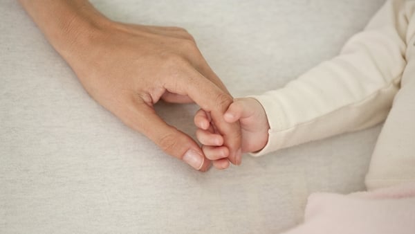 Close up image of a baby's hand gripping the finger of an adult