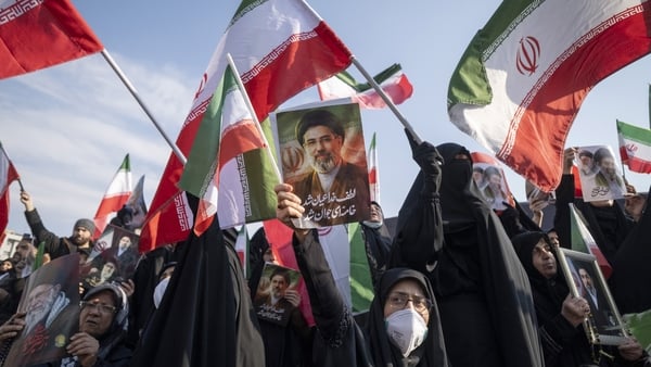 An Iranian woman wears a protective face mask and holds up a portrait of Iran's new Supreme Leader