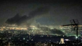 black smoke rises above a city skyline at night