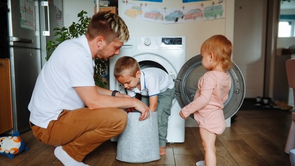 tired middle-aged dad loads the washing machine with two sibling children