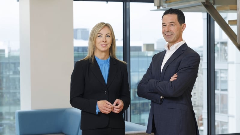 A business man and woman pose for a photo in a high rise office building