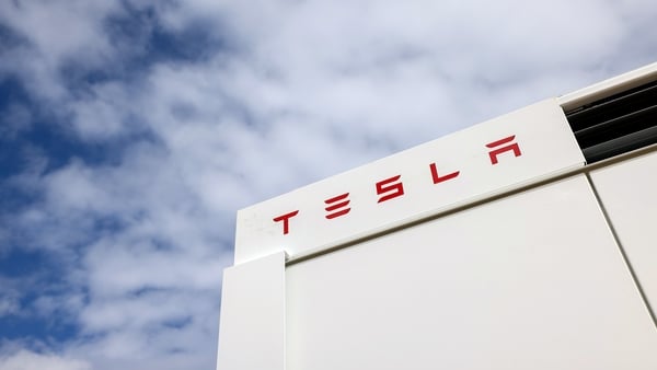 Tesla signage on a white building with a blue, cloudy sky in the background