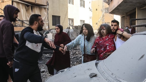 a woman in a read dress with blood and dust on her face is helped by other people after an airstrike in lebanon 