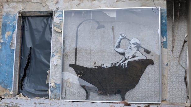 A protective glass case seals the art piece that features a bearded man having a bathcreated by British artist Banksy on the wall of a five-storey apartment building
