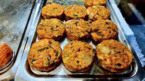 Freshly prepared salmon fish patties displayed on a metal tray at a market stall. The patties are made with salmon, herbs, and spices, ready to cook or grill. A popular seafood option in Nordic cuisine, rich in protein and omega-3 fatty acids.