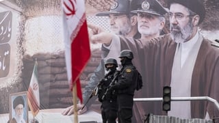 Two armed police officers stand guard in front of a giant banner depicting a portrait of Iran's new Supreme Leader, Ayatollah Mojtaba Khamenei, and military commanders