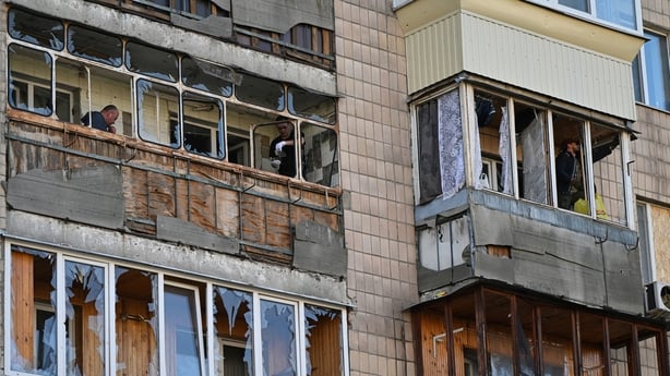People clear shattered glass on balconies in a damaged residential building in Kyiv