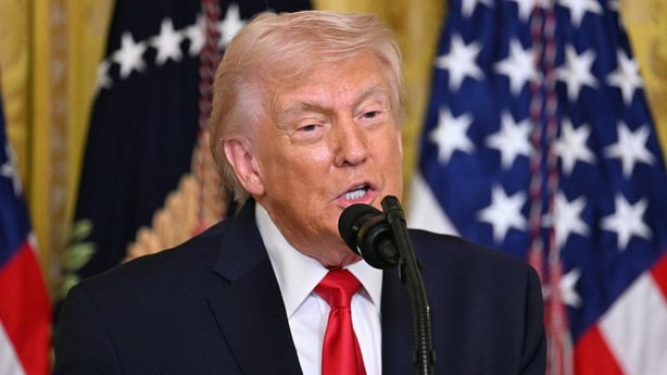 US President Donald Trump stands in front of an American flag.