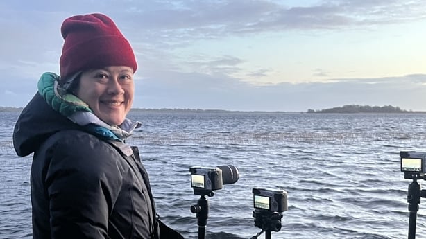Woman standing behind cameras on tripods facing out over a body of water