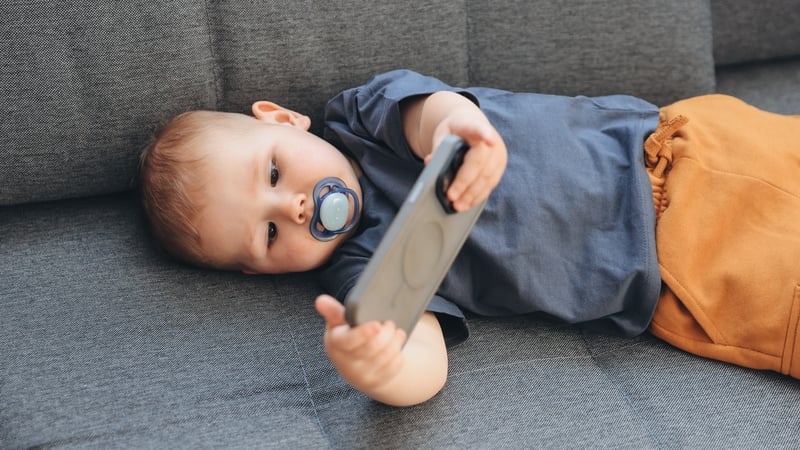 Baby boy with soother using mobile phone while lying on sofa at home
