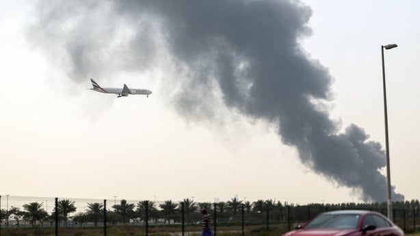 An Emirates Boeing 777 aircraft prepares for landing as a smoke plume rises from an ongoing fire near Dubai International Airport in Dubai on March 16, 2026
