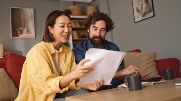 Happy couple sitting on couch, reviewing life insurance documents and planning their future (Getty Images)