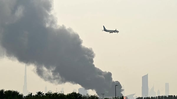 An Emirates aircraft flies past plumes of smoke from an ongoing fire near Dubai International Airport