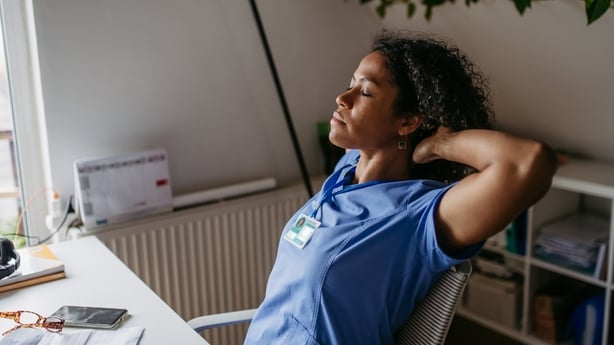 Female doctor having a break in her office, sitting with hands behind head and closed eyes, relaxing for moment. Having cup of coffee in work.