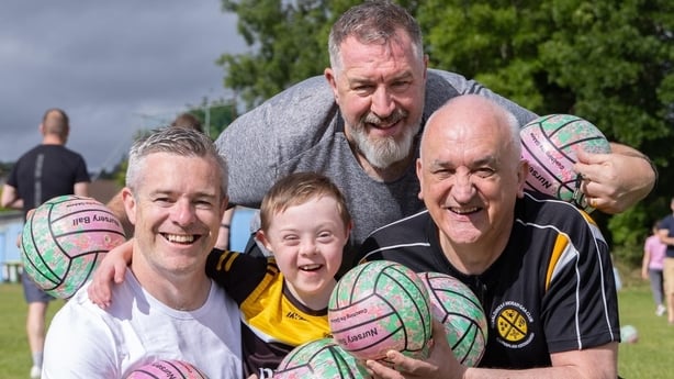 GAA coaches pose with a young player holding footballs.