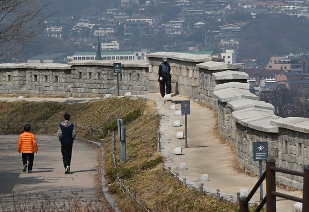 People walk along the fortress wall at Naksan Park in Seoul on 17 March , 2026. (Photo by Jung Yeon-je / AFP) / TO GO WITH AFP STORY SKorea-tourism-entertainment-animation BY Kang Jin-kyu