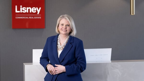 A business woman poses for a picture with a sign for Lisney behind her